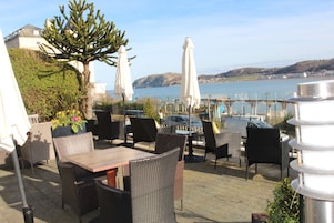 An outdoor patio with wicker furniture, umbrellas, and a view of the sea.