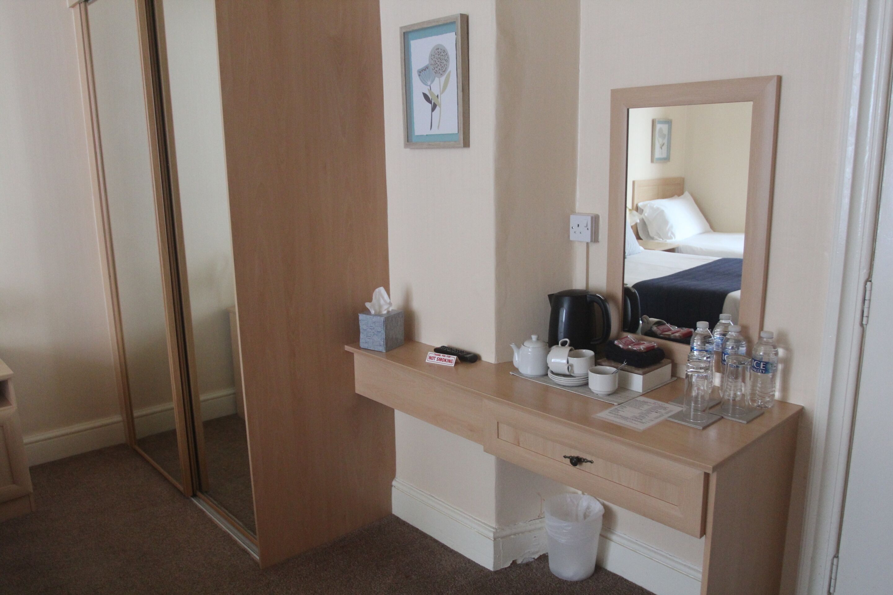 Una habitación de hotel con un escritorio de madera, un espejo, una cama y un pequeño cubo de basura.