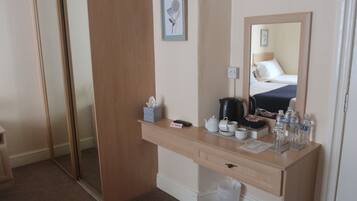 Una habitación de hotel con un escritorio de madera, un espejo, una cama y un pequeño cubo de basura.
