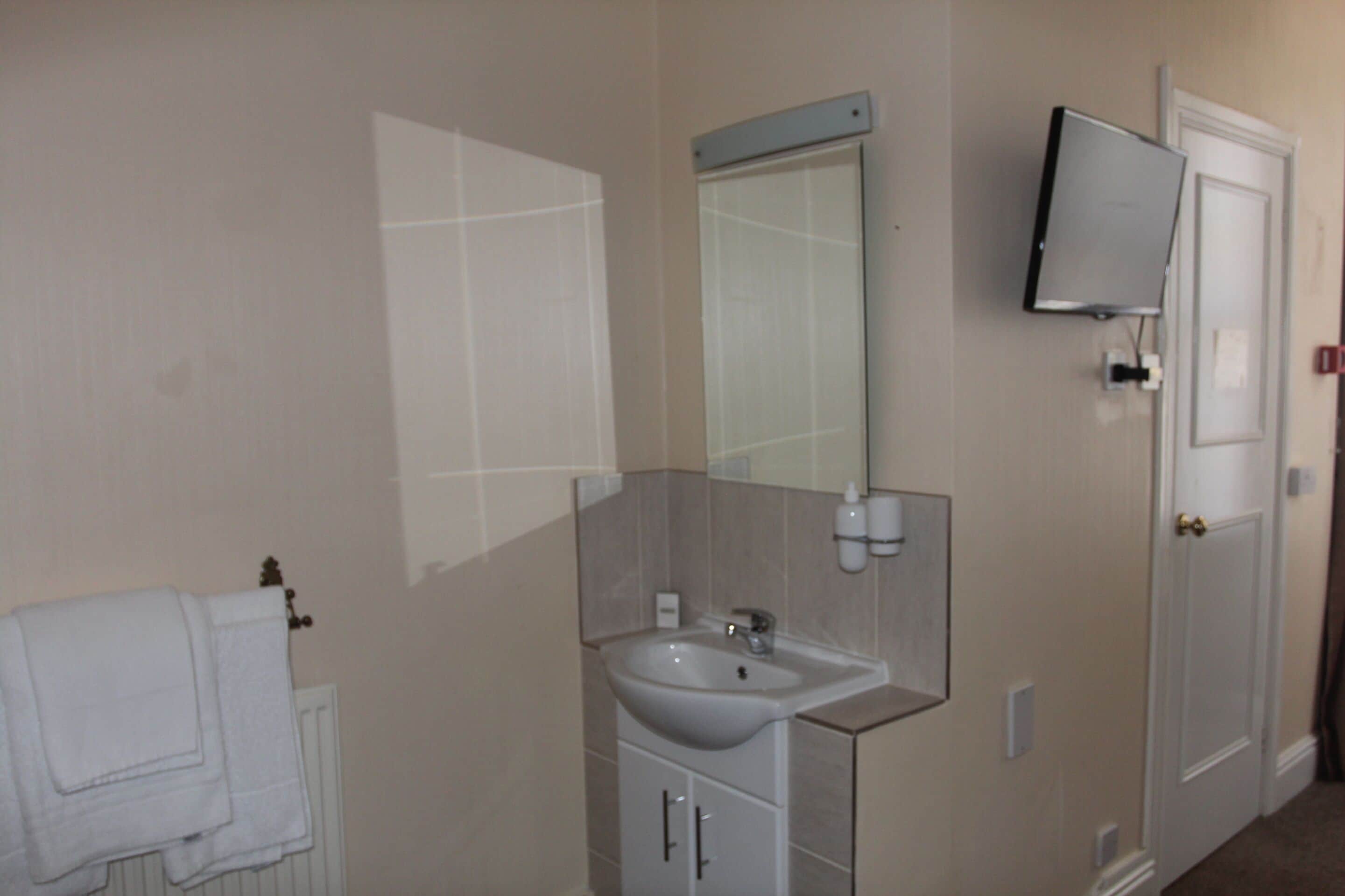 Un baño con lavabo, espejo, toallero y puerta.