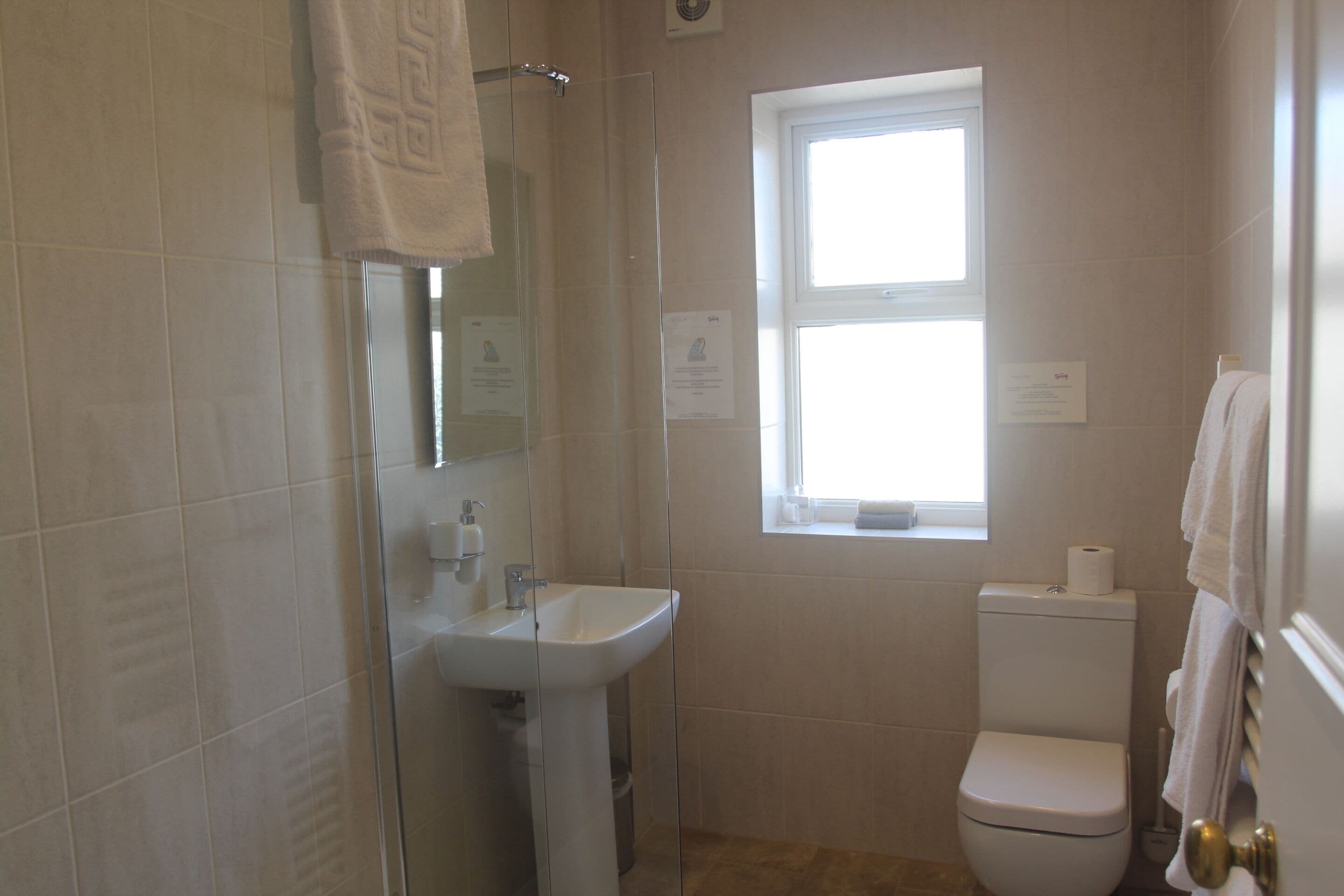 A bathroom with a glass shower enclosure, a white sink, a toilet, and a window providing natural light.