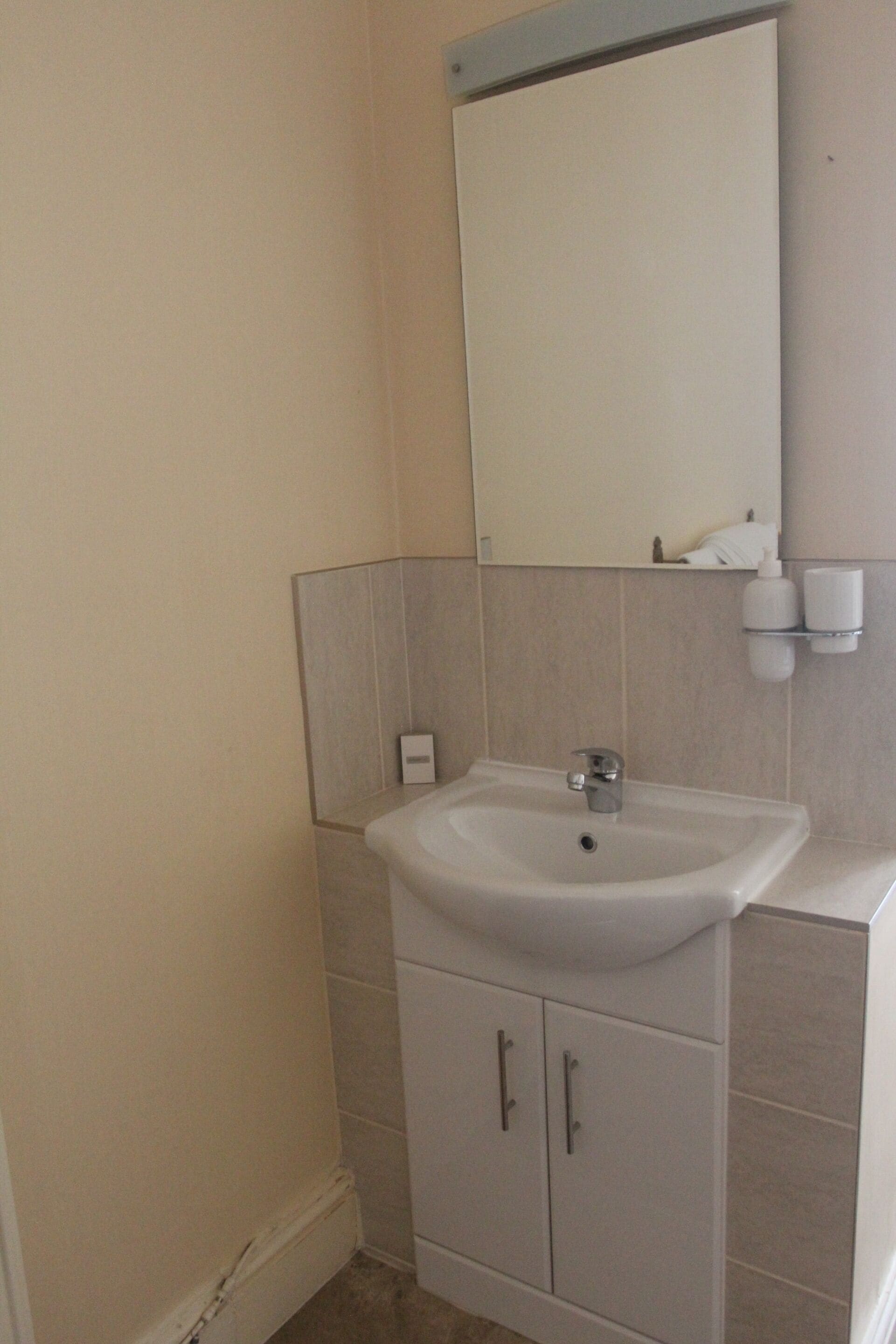 A bathroom with a white sink, mirror, and cabinets.