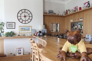 A bar area with a wooden counter, chairs, a clock, and a decorative frog statue.