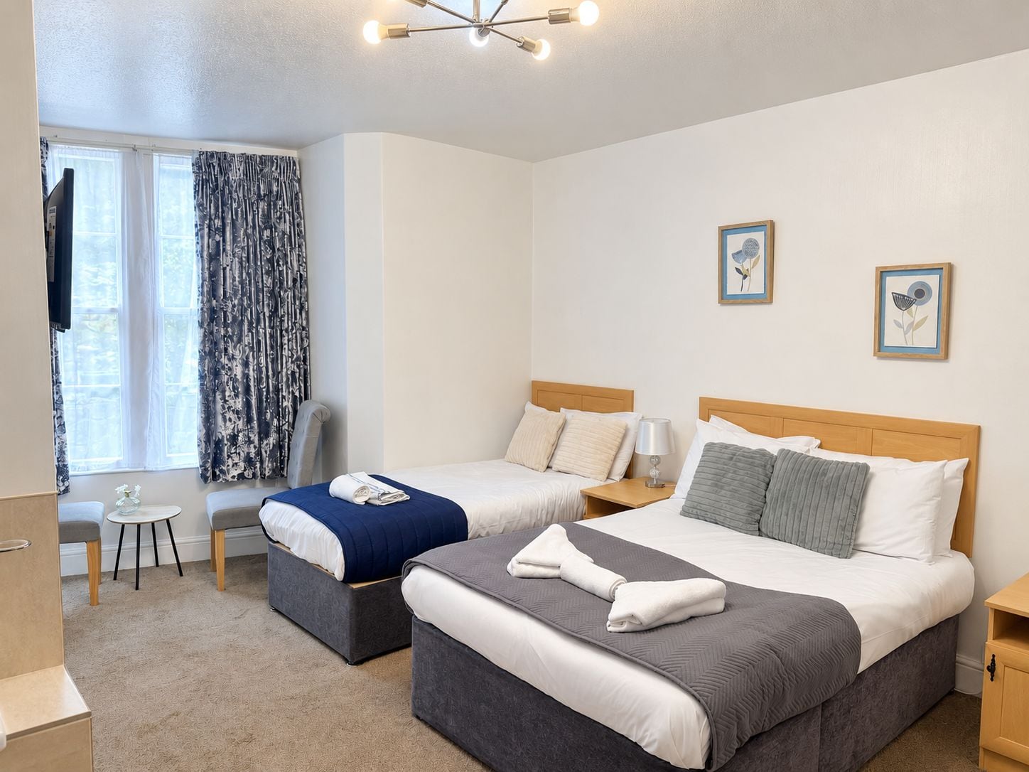A hotel room with two beds, a desk, a chair, and a TV.