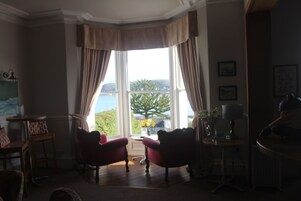 A corner room with two red armchairs, a small table with a lamp, and a view of the sea through large windows.