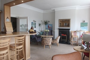 A room with a bar area, seating, a fireplace, and artwork on the walls.