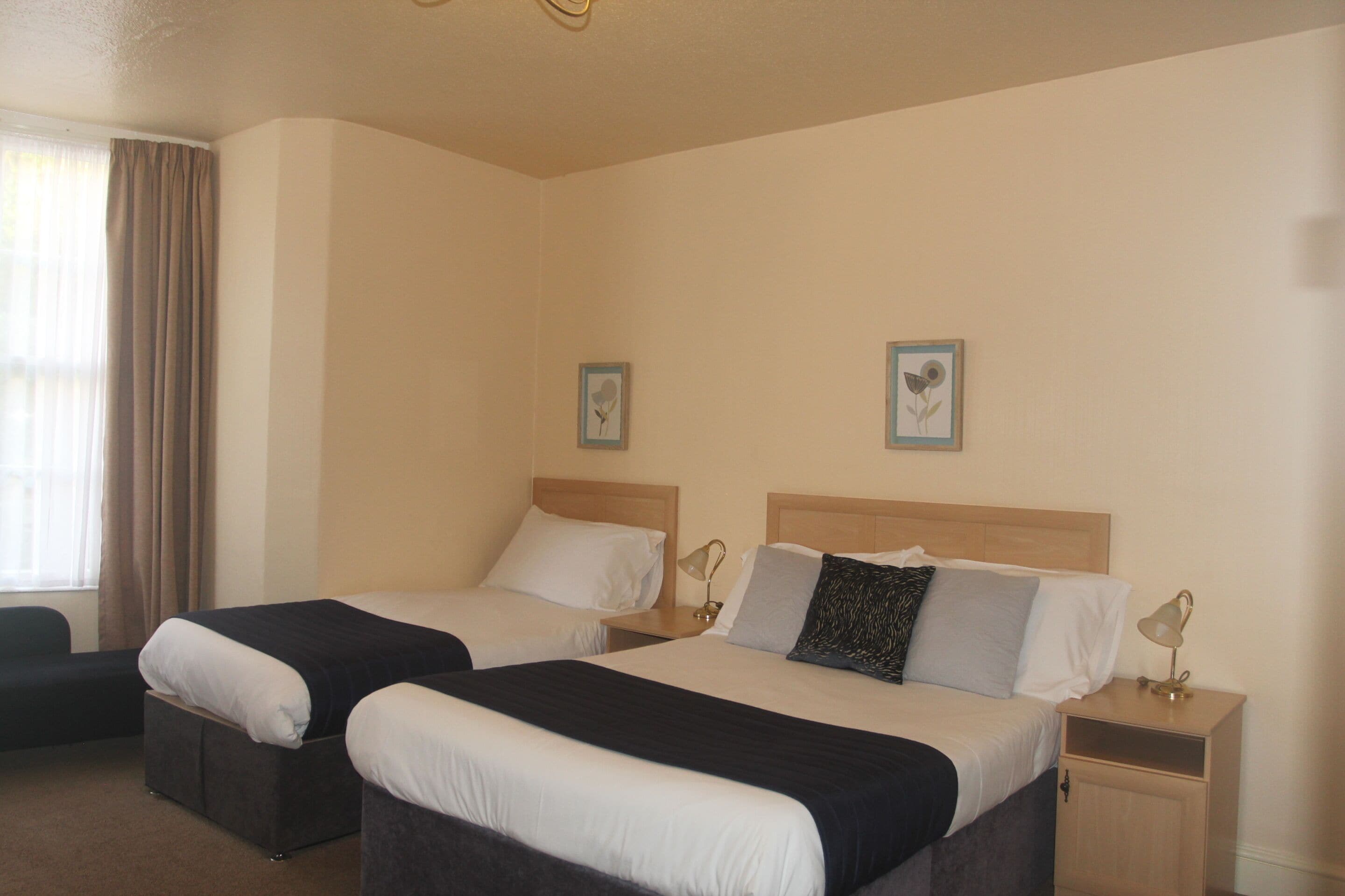 A hotel room with two single beds, a small desk, and a chair.