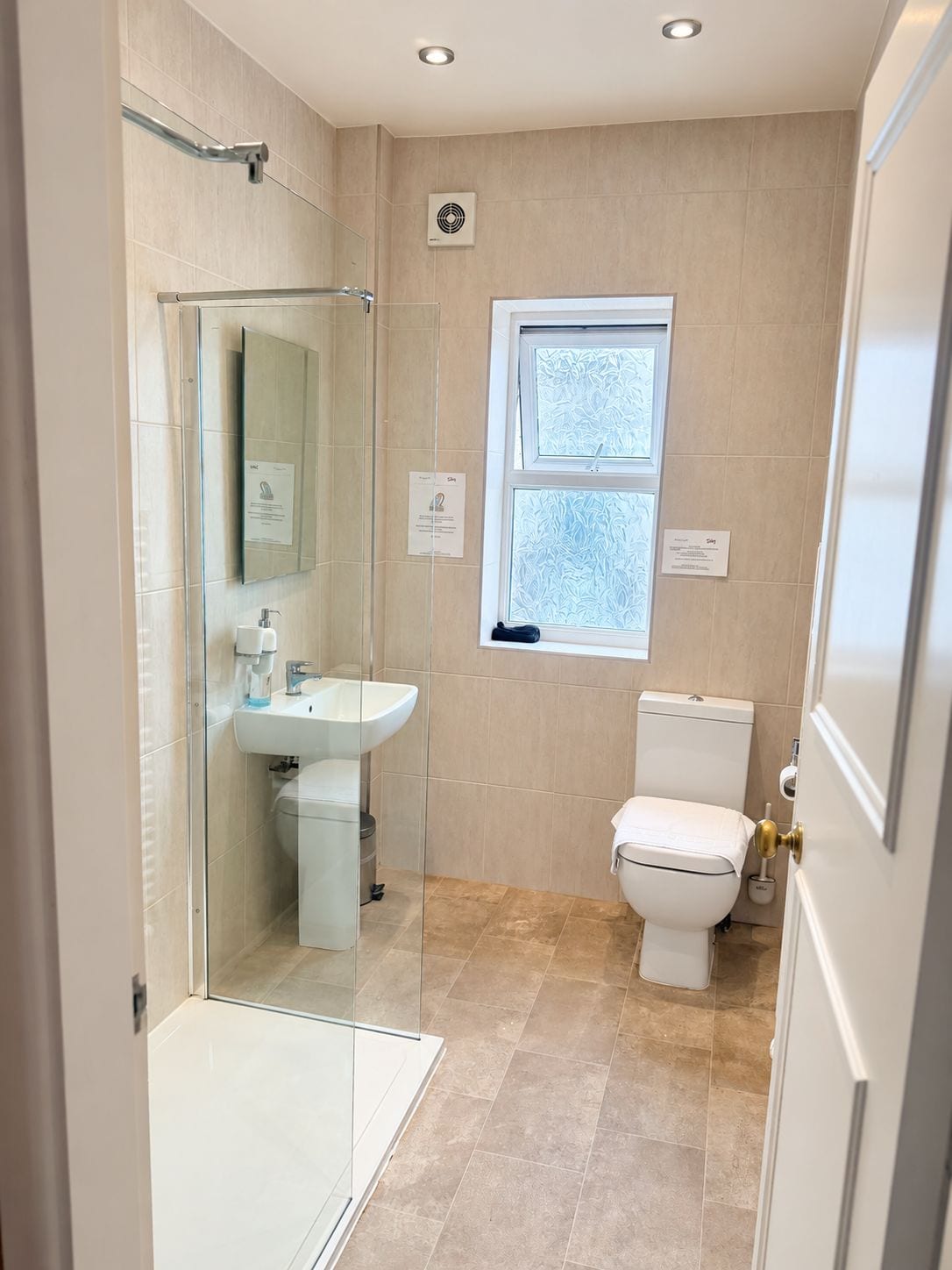 A modern bathroom with a glass shower enclosure, a white sink, a toilet, and a window.