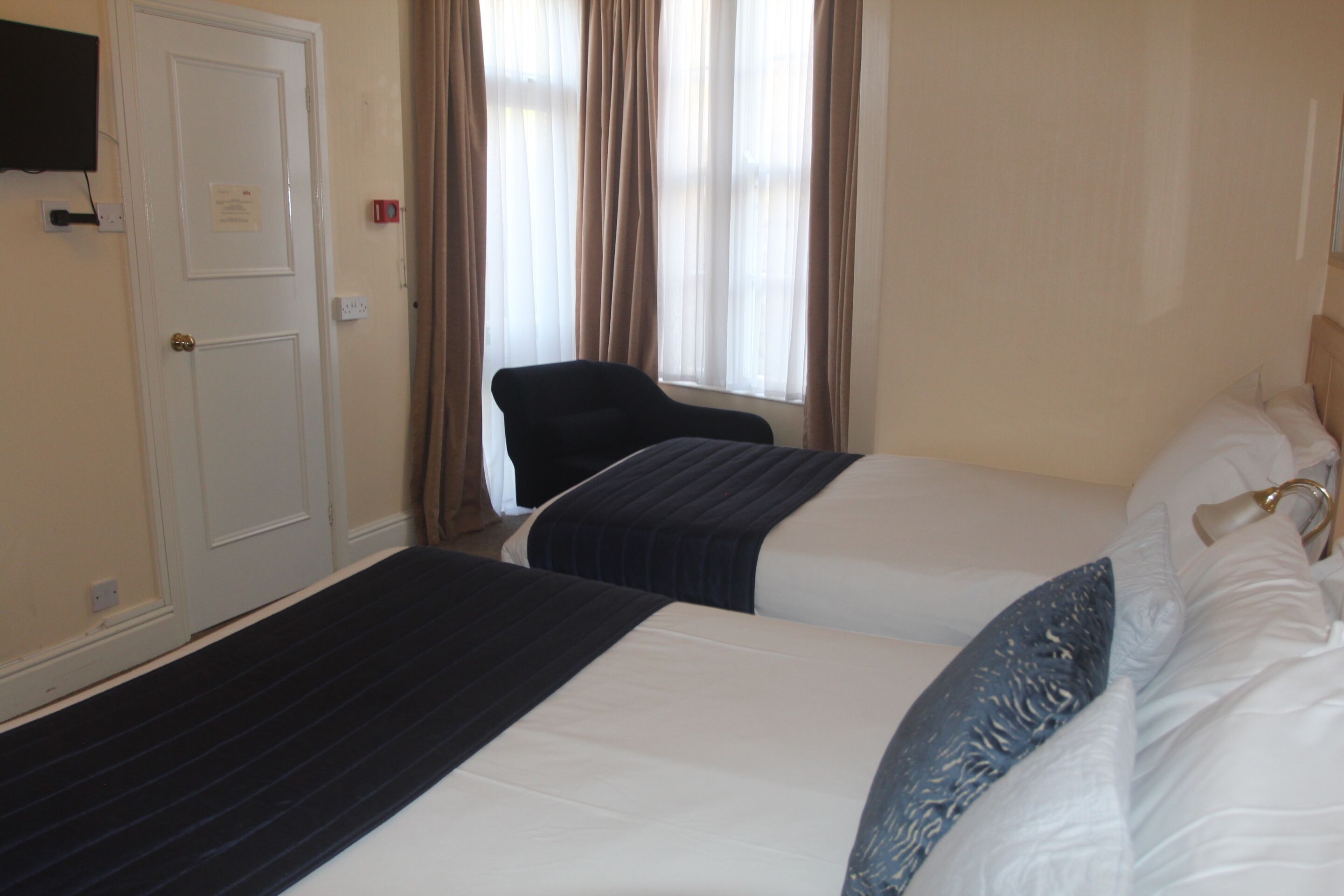 A hotel room with two beds, a chair, a door, and a window with curtains.