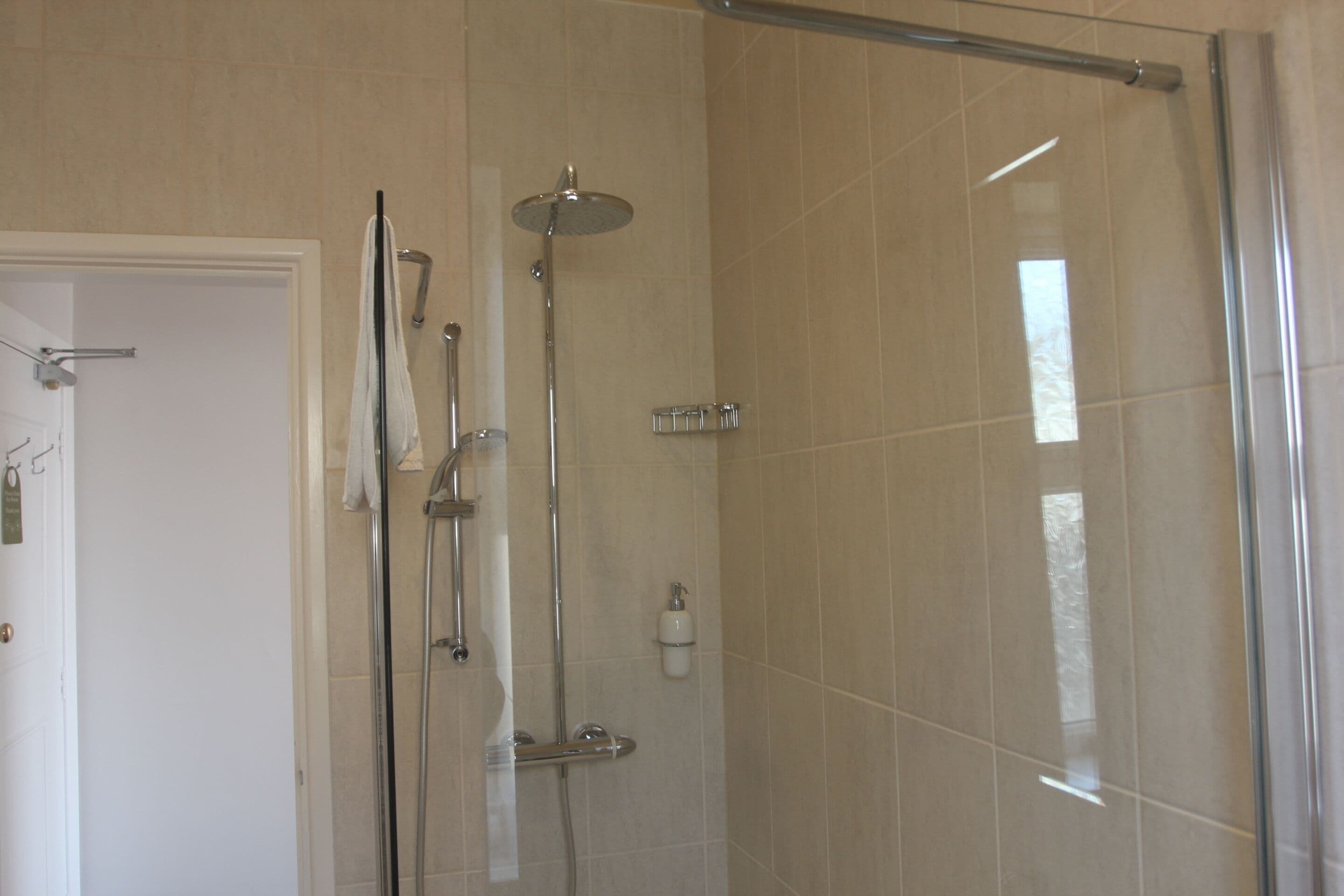 A modern bathroom with a glass shower enclosure, a white door, and a towel rack.