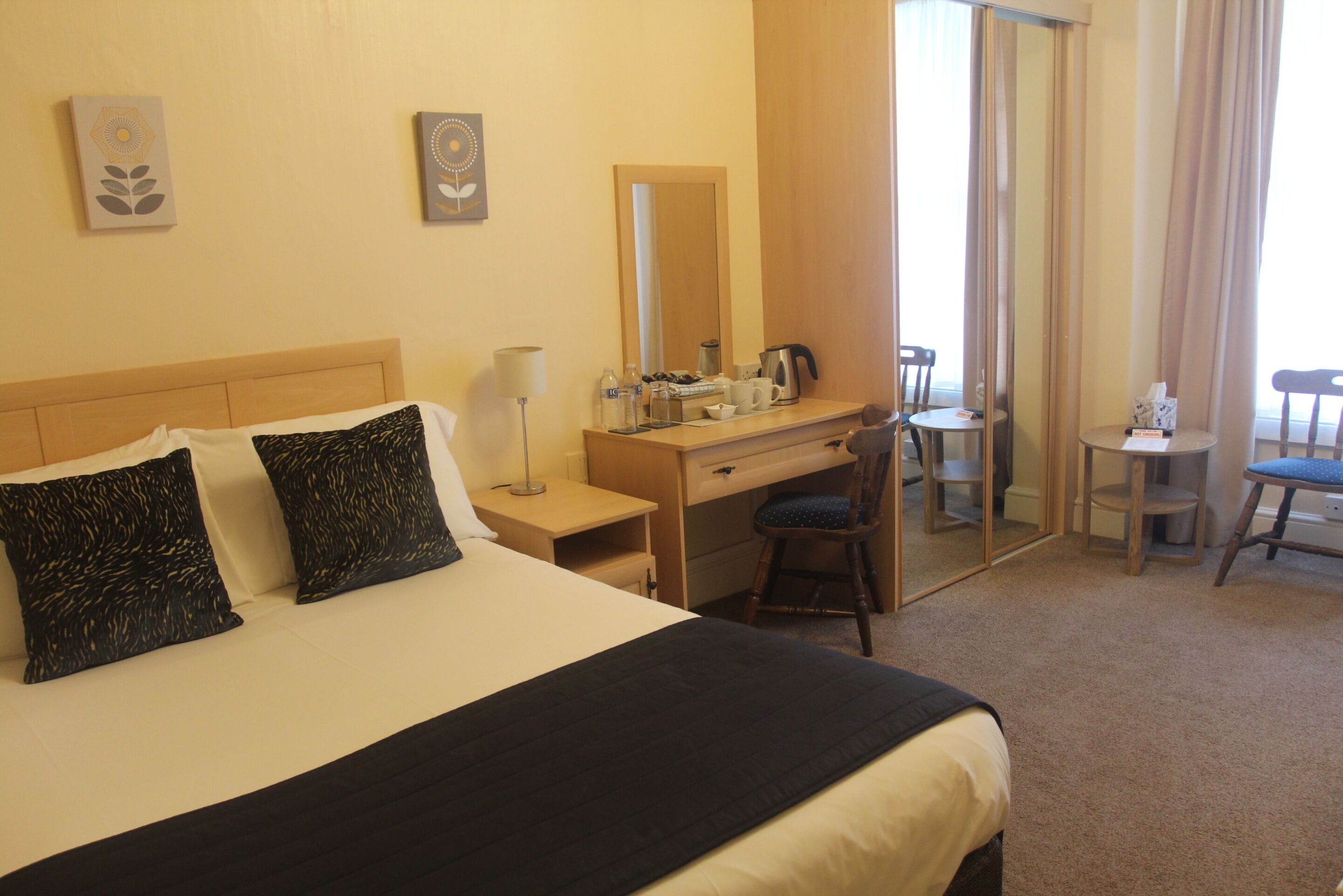 Une chambre d’hôtel avec un lit, un bureau, une chaise, un miroir et une petite table.