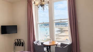 Habitación de hotel con cama, televisión montada en la pared, mesa con dos sillas y un ventanal con cortinas.