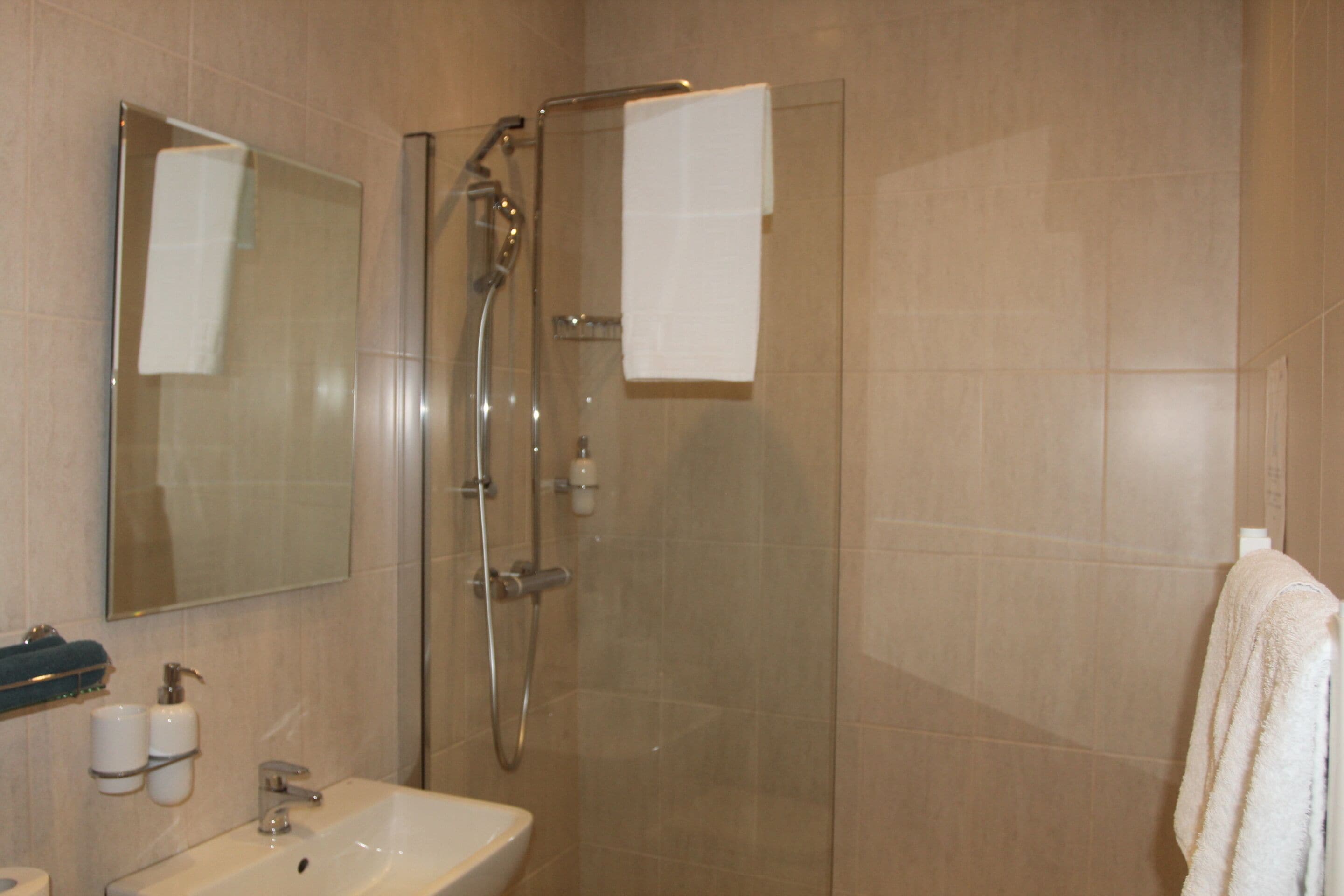 Un baño con ducha de mampara, lavamanos, espejo y dos toallas colgadas en la pared.