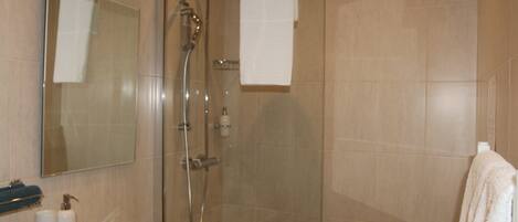 Un baño con ducha de mampara, lavamanos, espejo y dos toallas colgadas en la pared.
