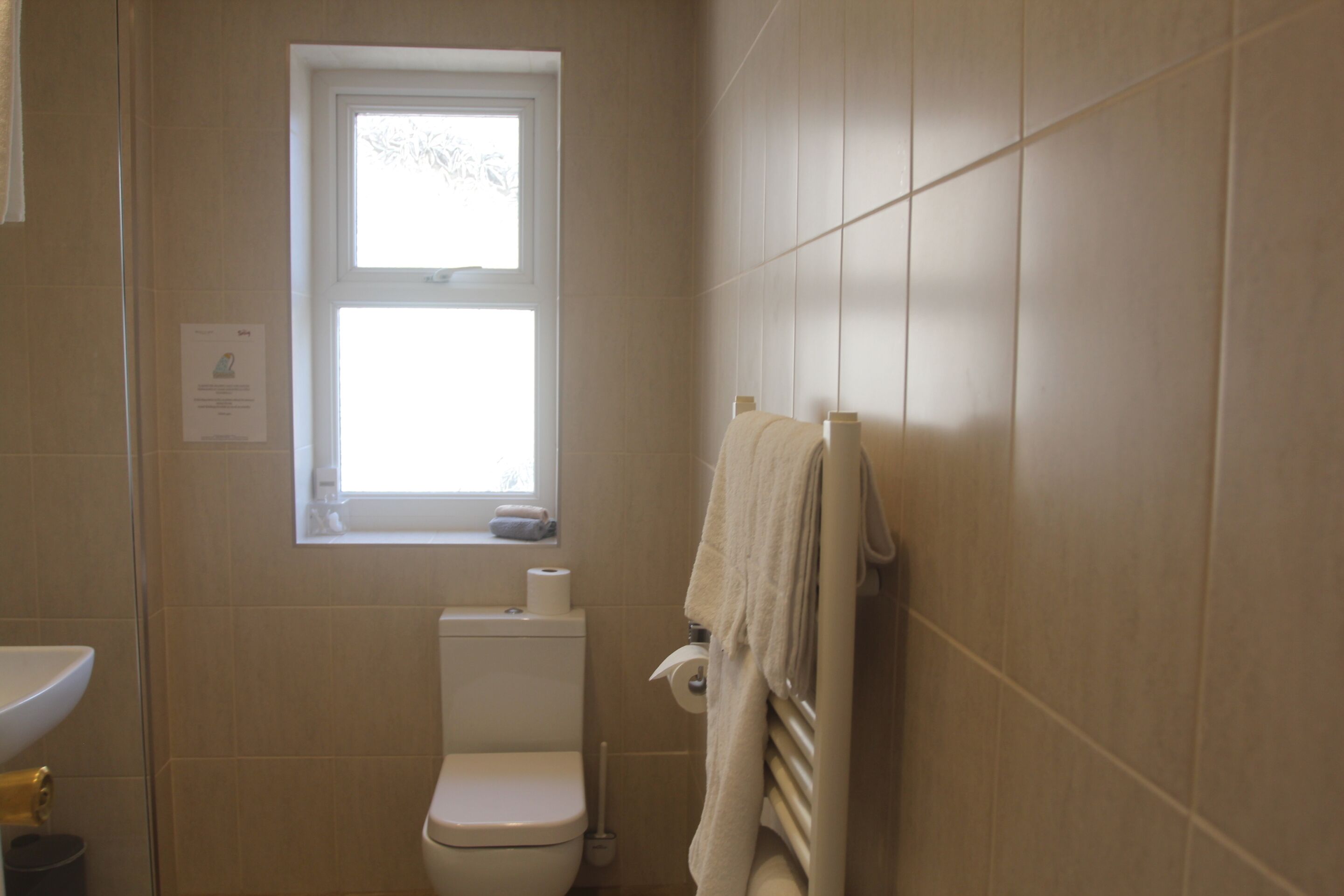 A small bathroom with a toilet, a window, and a towel rack.
