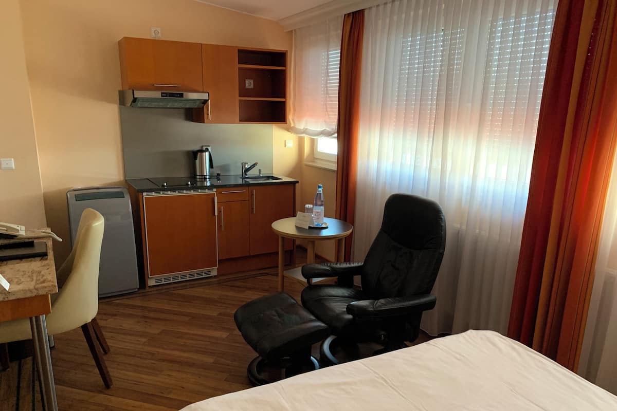 Een hotelkamer met een bed, een bureau met stoel, een kitchenette en een raam met gordijnen.
