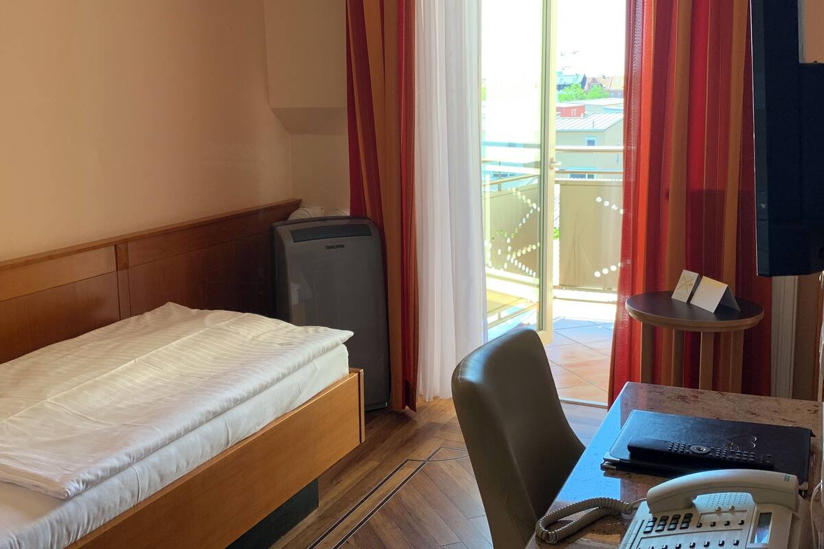 Een hotelkamer met een bed, een bureau met een telefoon, een stoel en een tafeltje met een boek en een bord.