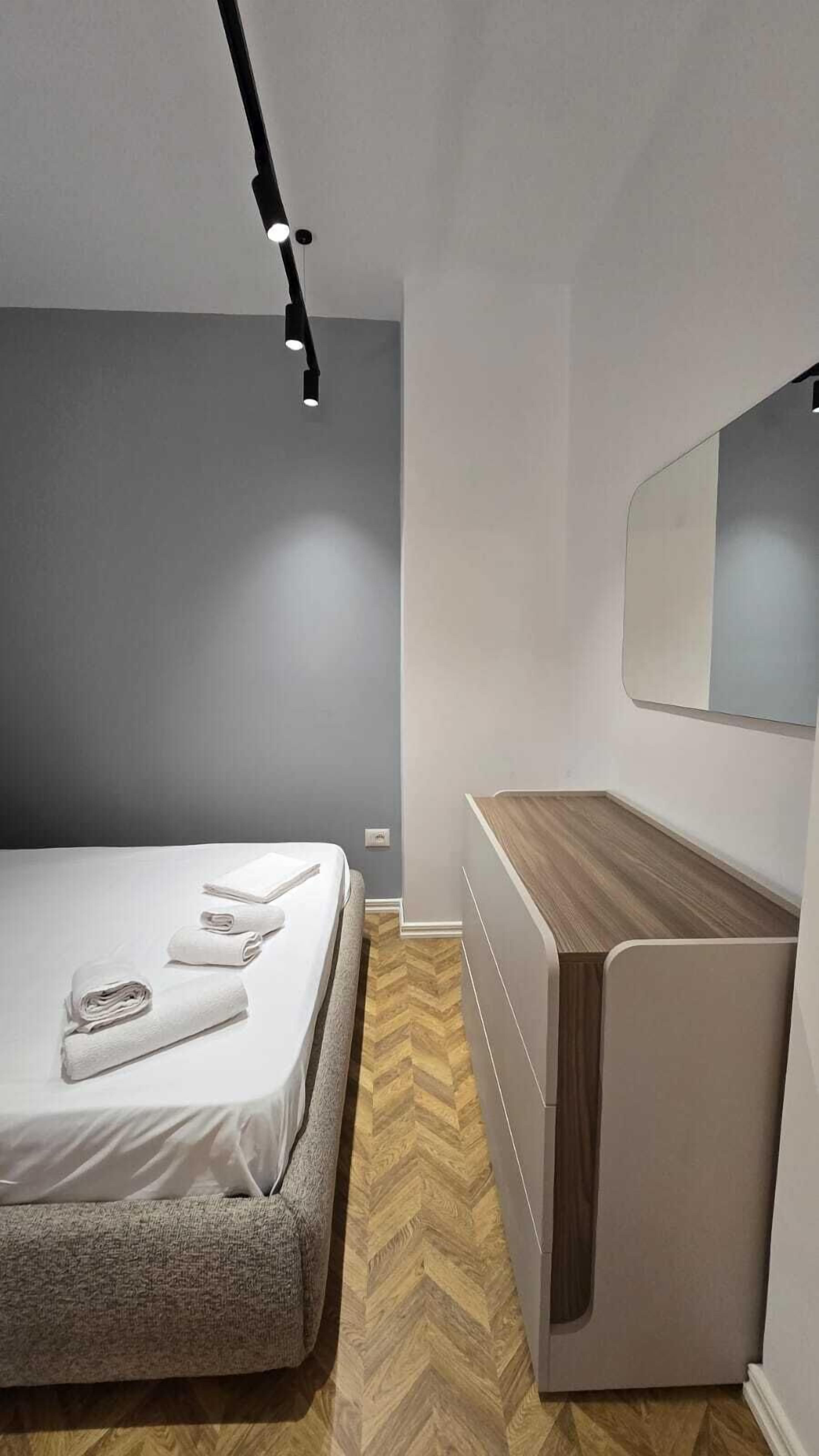 A modern bedroom with a bed, a bedside table, a mirror, and a ceiling light.