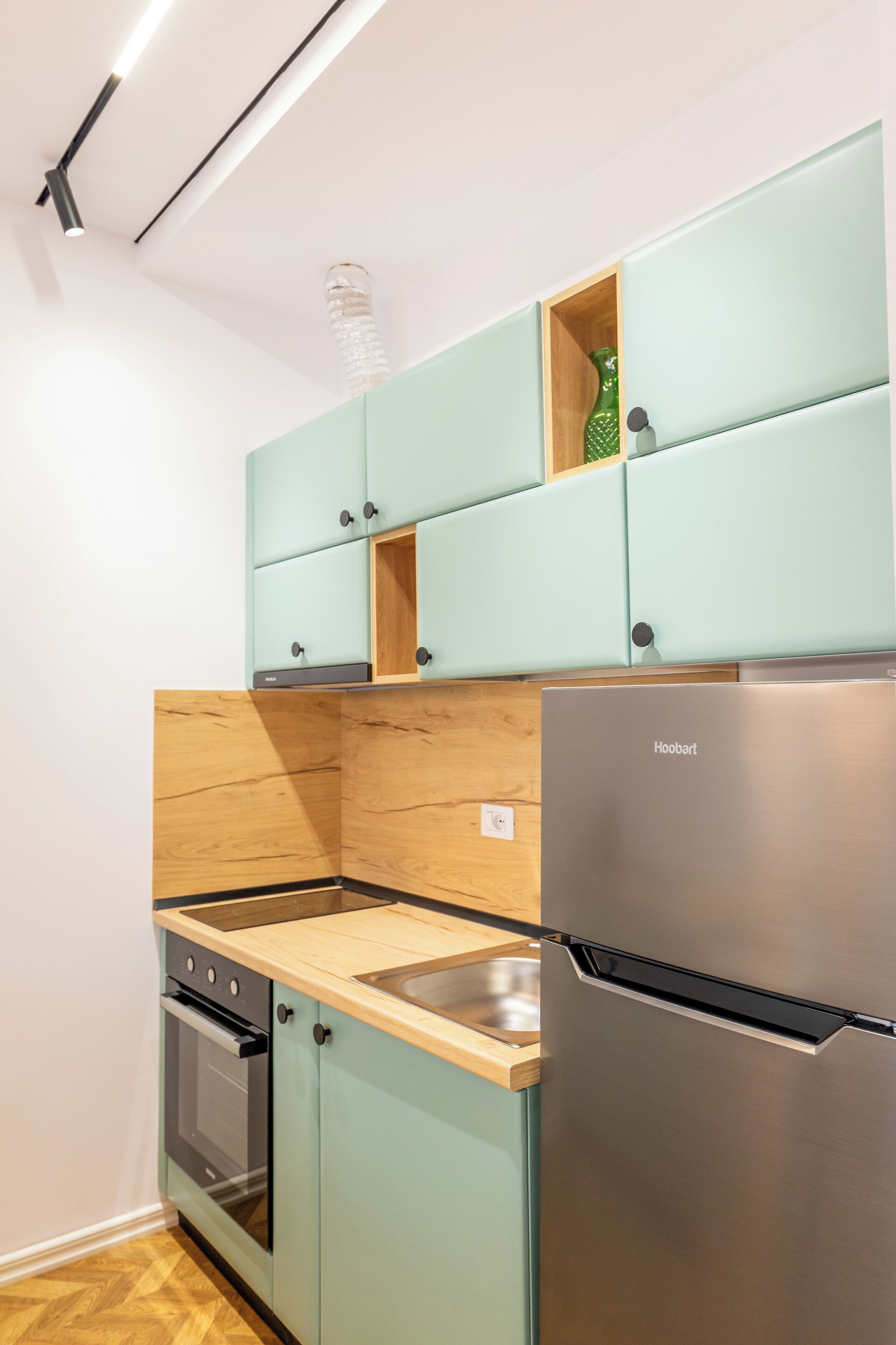Une cuisine compacte avec des meubles de couleur turquoise, un réfrigérateur en acier inoxydable et un plan de travail en bois.