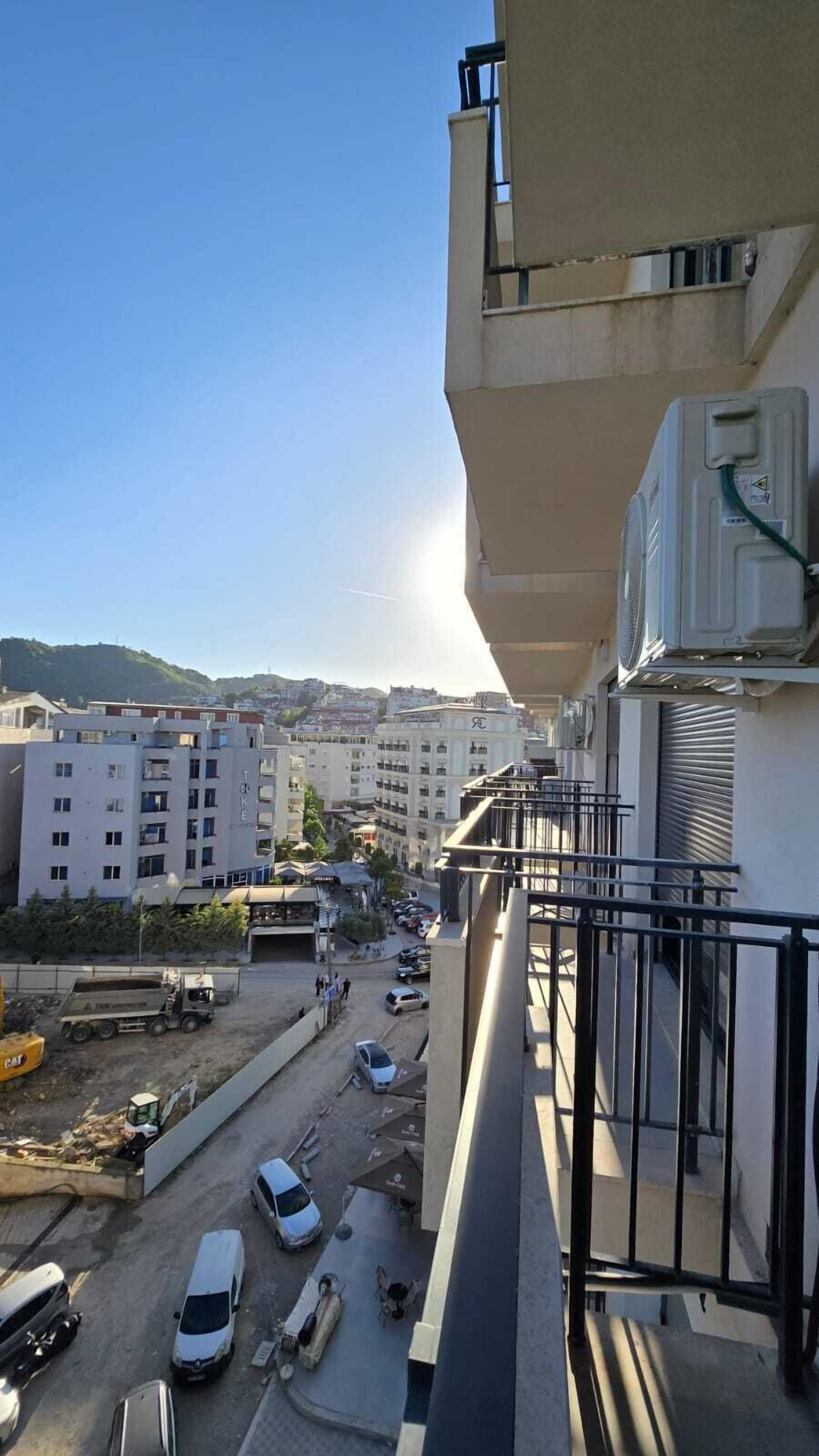Um edifício alto com várias varandas, dando para uma rua movimentada com carros estacionados e atividade de construção.