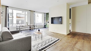 A modern living room with a sofa, coffee table, and TV. Large windows offer views of the outside. - Appartement Beaubourg (Paris)