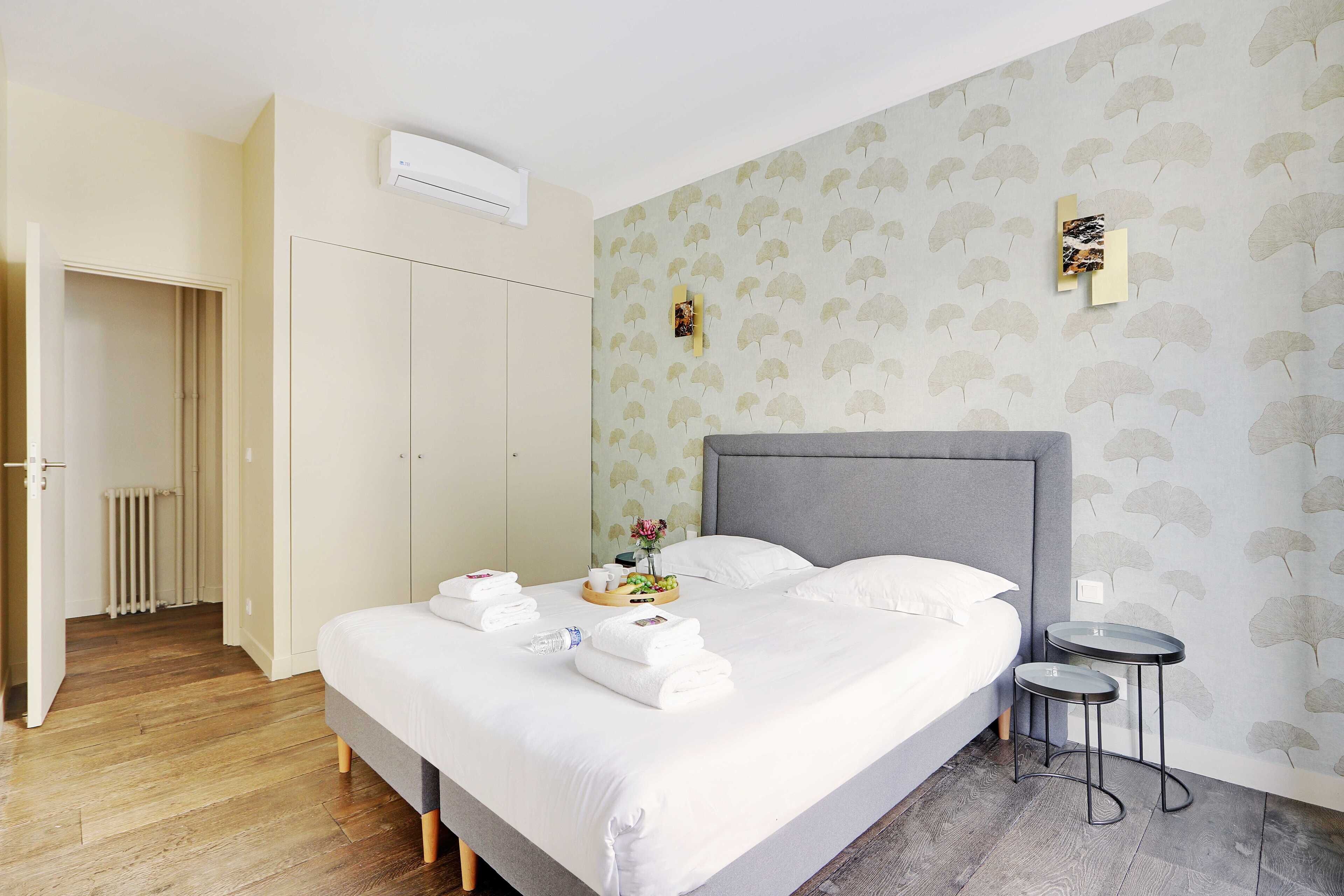 Een net opgemaakt bed met witte lakens, een grijs hoofdbord en twee nachtkastjes.