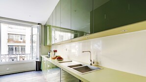 A modern kitchen with a large window, a sink, and green cabinets. - Appartement Beaubourg (Paris)