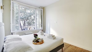 A hotel room with a large bed, a window with a view of trees, and a tray with towels and a vase of flowers. - Appartement Beaubourg (Paris)