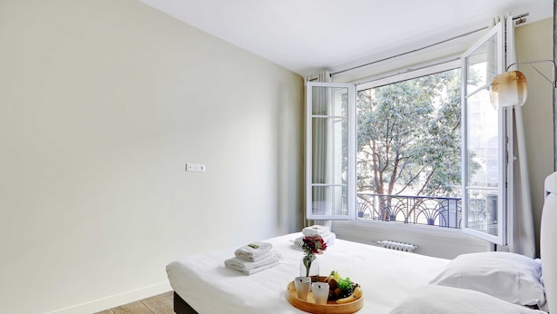 A neatly made bed with white linens, a tray with fruits and a vase of flowers, and a view of trees through an open window. - Appartement Beaubourg (Paris)