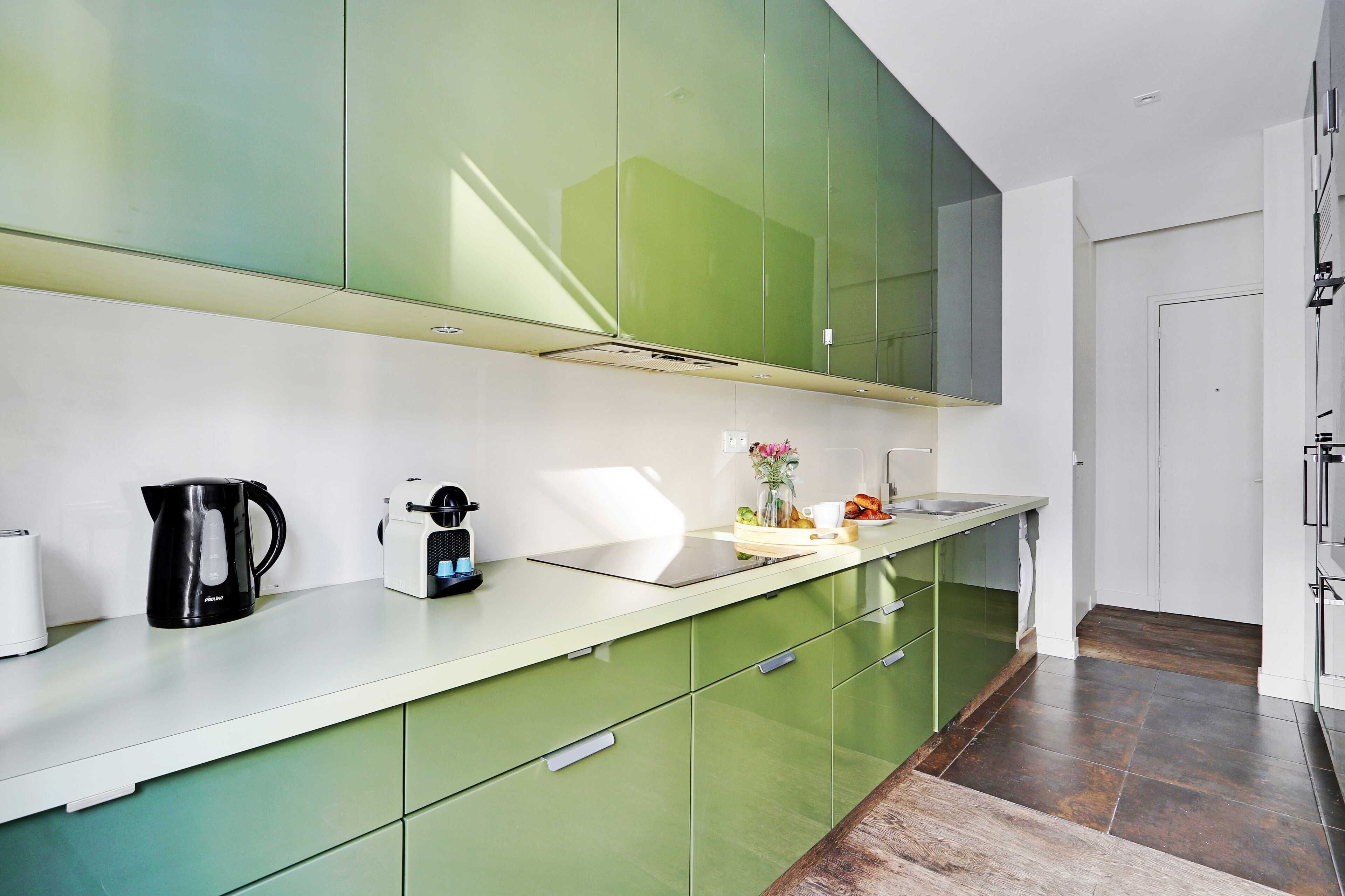 Une cuisine moderne avec des meubles de couleur verte, un plan de travail blanc et une machine à café.