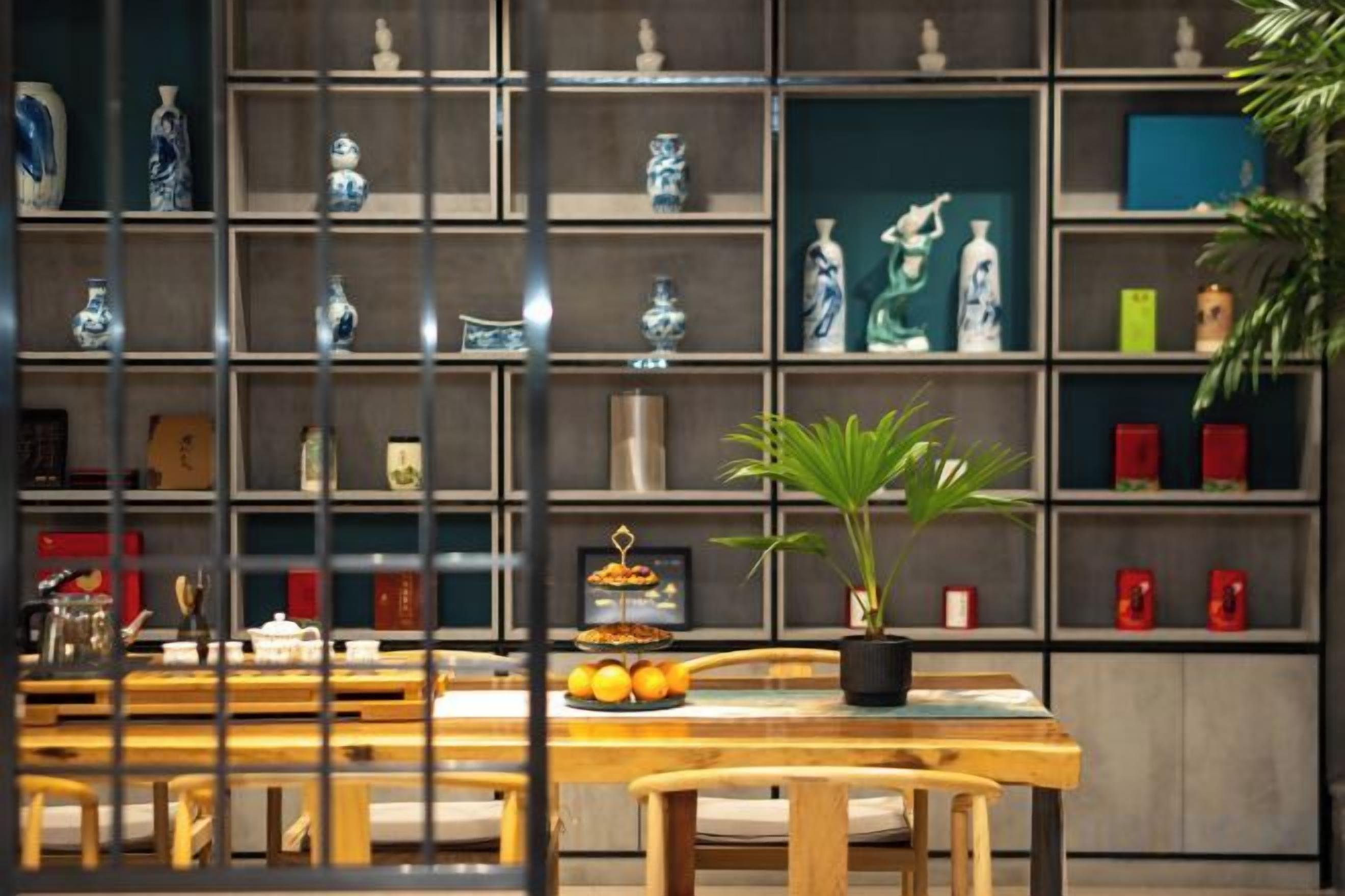 A room with a wooden dining table, chairs, a potted plant, and shelves with decorative items.