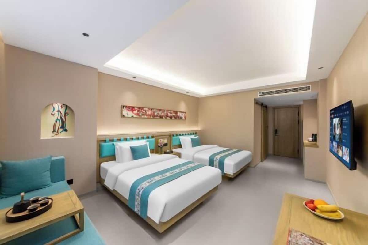 Ein Hotelzimmer mit zwei Betten, einem Schlafsofa, einem Esstisch und Bildern an der Wand.