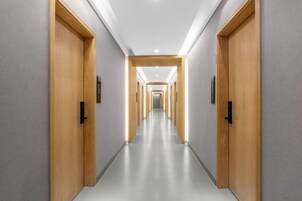 Un pasillo largo y estrecho con puertas de madera a ambos lados y suelo de color claro.