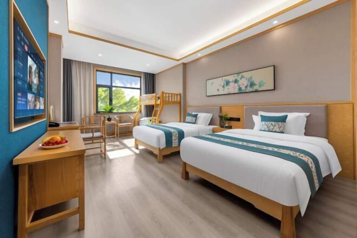 Ein Hotelzimmer mit zwei Betten, einem Schreibtisch mit Obst, einem Sessel und einem großen Fenster.