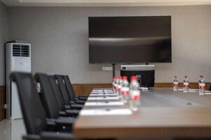 Una sala de conferencias con una larga mesa, sillas, un televisor de pantalla plana y botellas de agua.