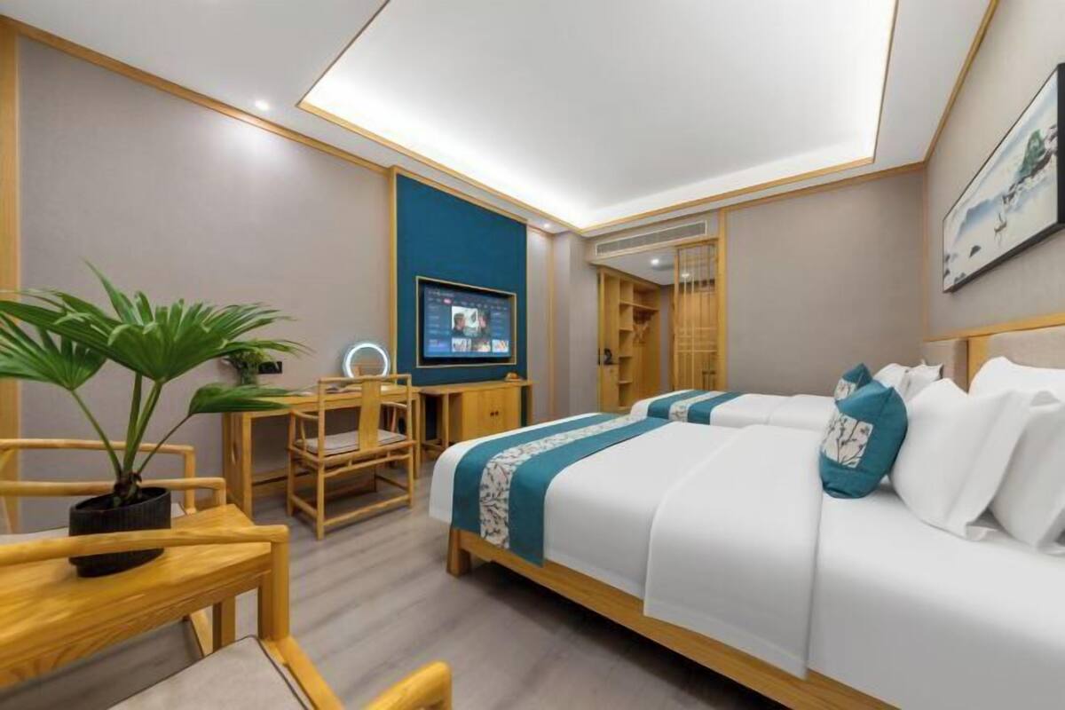 Ein Hotelzimmer mit Bett, Schreibtisch, Stuhl, Fernseher und einer Zimmerpflanze.
