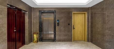 A hallway with a marble floor, a wooden door, and an elevator with a glass door.