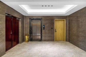 Un couloir doté d’un sol en marbre, d’une porte en bois et d’un ascenseur à porte vitrée.