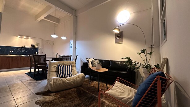 Een moderne woonkamer met een bank, fauteuil en een salontafel. Achtergrond is een eethoek met een zichtbare keuken.