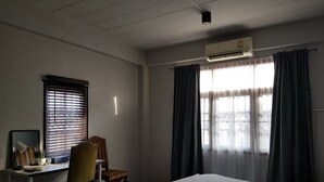 Een hotelkamer met een bed, een bureau met stoel, een raam met gordijnen en een airconditioning.