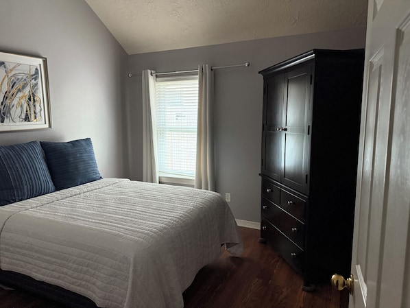 A bedroom with a bed, a wardrobe, a window with curtains, and a painting on the wall.