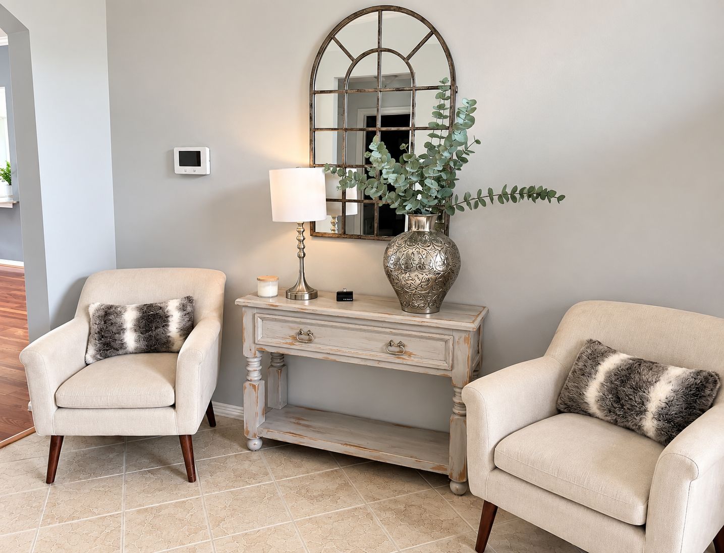 A room with two armchairs, a white console table, a mirror, a lamp, and a vase with a plant.