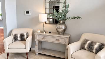 A room with two armchairs, a white console table, a mirror, a lamp, and a vase with a plant.