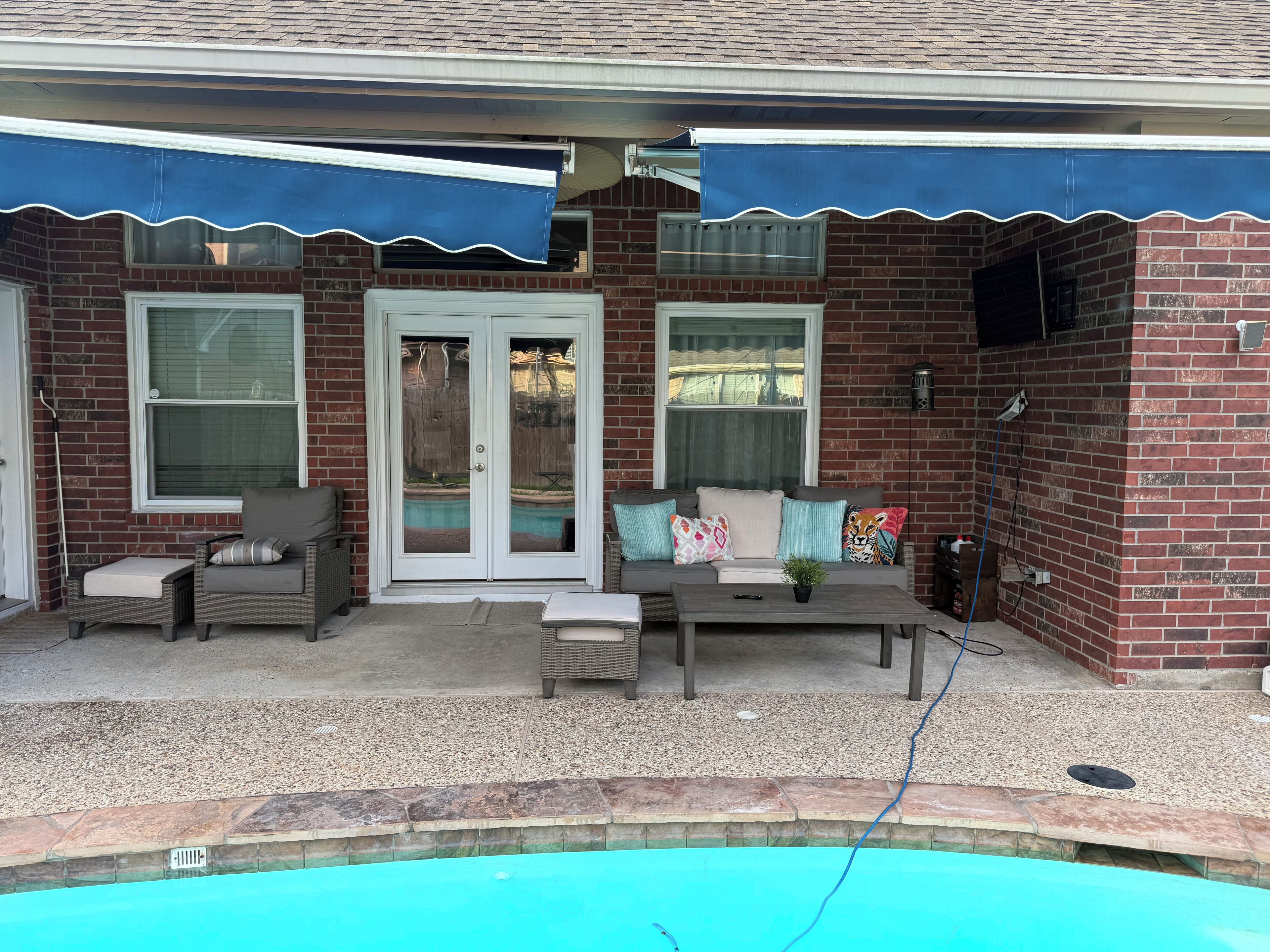 A covered patio area with a pool, outdoor seating, and a brick wall.