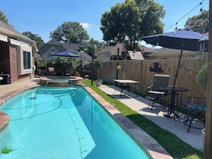 A backyard with a swimming pool, patio furniture, and a wooden fence.