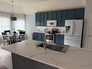 A modern kitchen with a central island, a dining area with chairs, and a microwave above the cabinets.