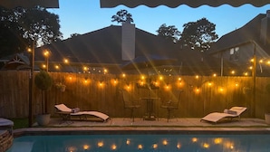 A swimming pool with a wooden deck, lounge chairs, and string lights. - House of blue! Beautiful pool, near IAH airport (Humble)