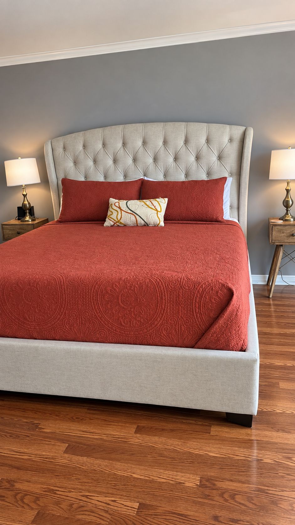 Uma cama com cabeceira estofada, roupa de cama vermelha e duas luminárias laterais.