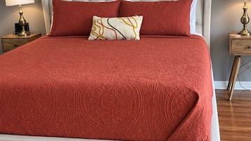 Een bed met een gebutste hoofdbord, rode beddengoed en twee bedlampjes.