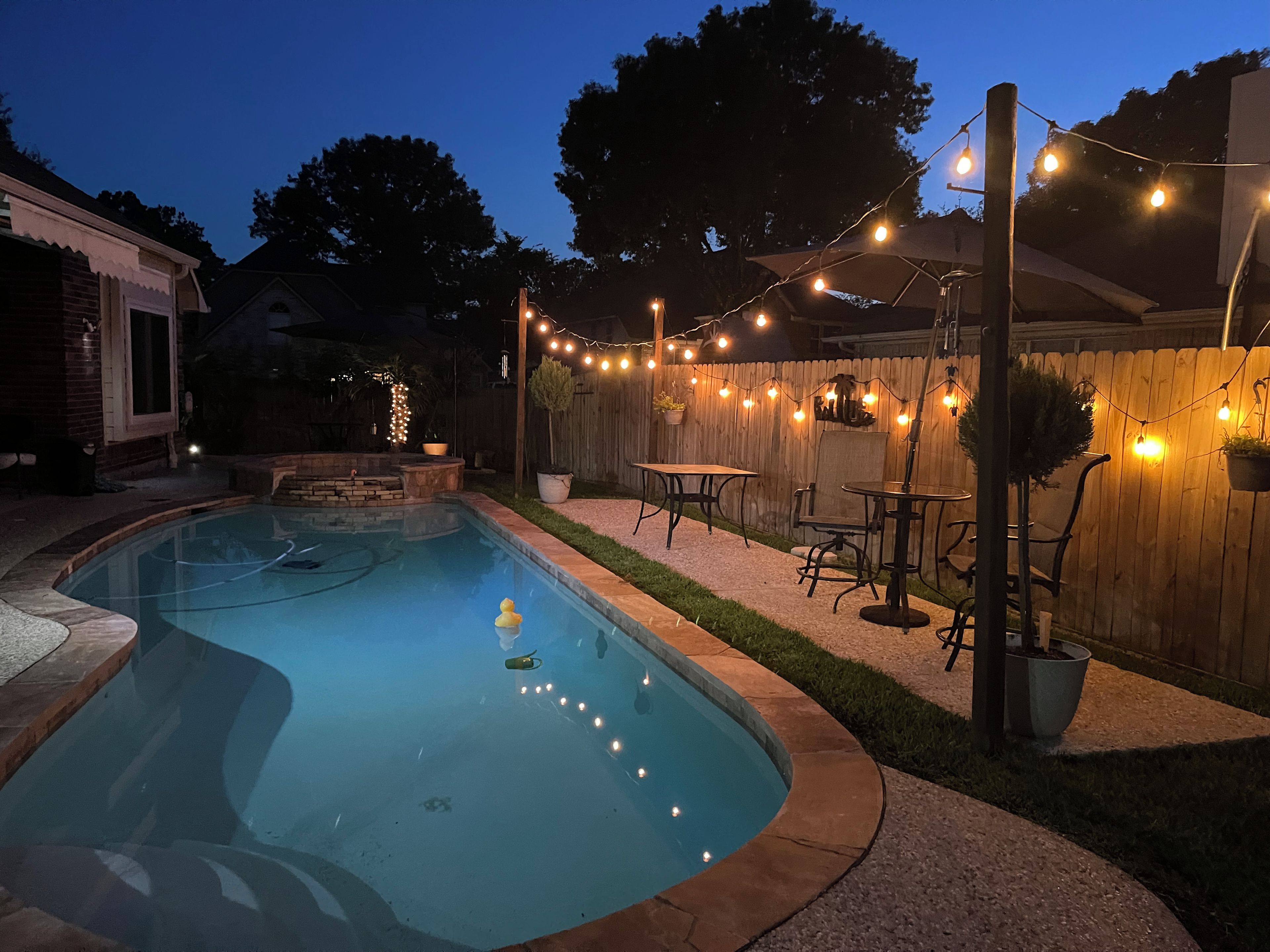Un jardin avec une piscine, des meubles d’extérieur et des guirlandes lumineuses.